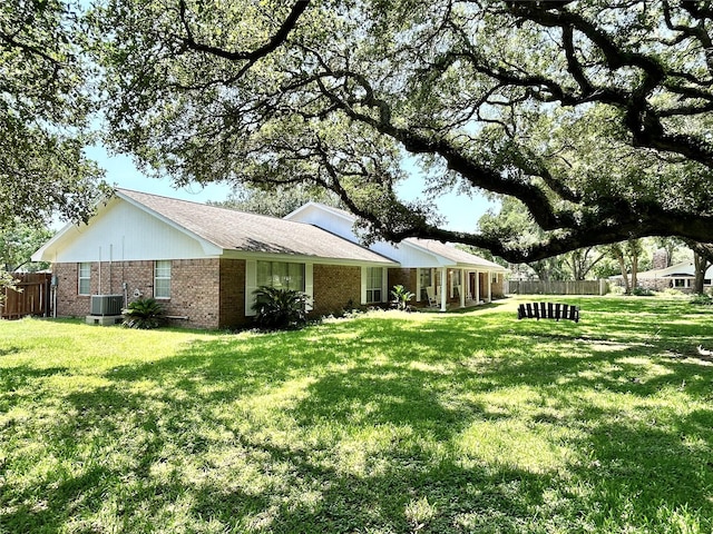 view of side of home featuring cooling unit, a lawn, fence, and brick siding