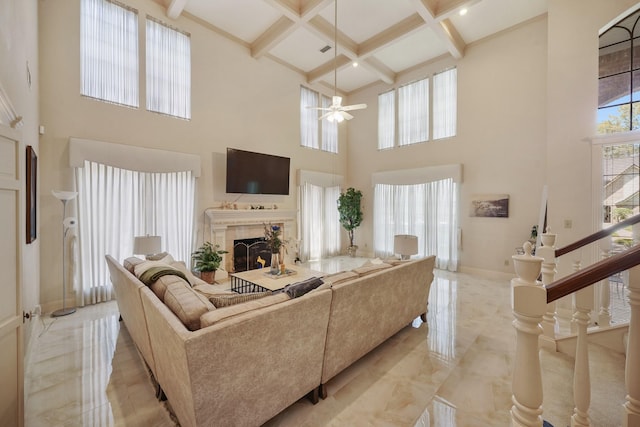 living room with beam ceiling, coffered ceiling, a ceiling fan, a high ceiling, and a fireplace