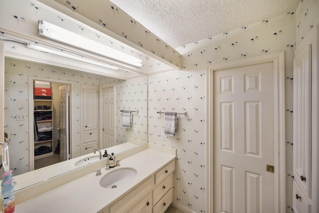 bathroom with wallpapered walls, vanity, a textured ceiling, and a closet