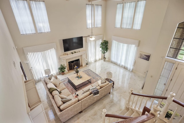 living area featuring marble finish floor, a ceiling fan, a towering ceiling, and a premium fireplace