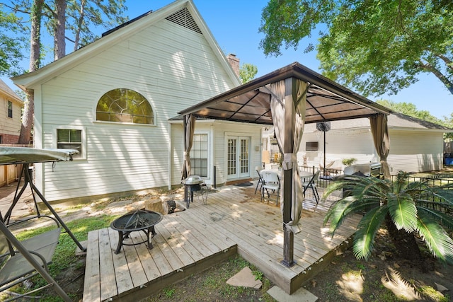 rear view of house with french doors, a fire pit, a gazebo, a deck, and outdoor dining space