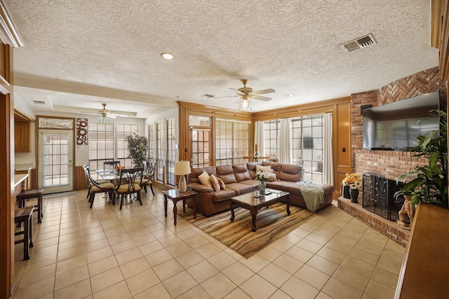 living room featuring a ceiling fan, a brick fireplace, light tile patterned flooring, and visible vents
