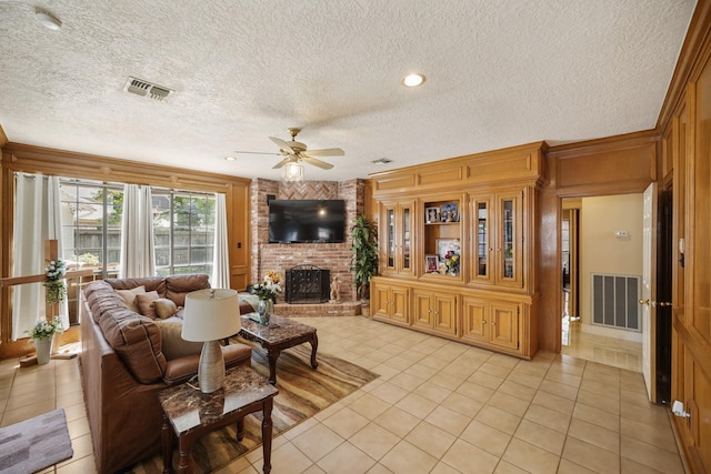 living area featuring light tile patterned flooring, a brick fireplace, visible vents, and a ceiling fan