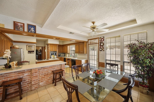 dining room featuring a textured ceiling, light tile patterned floors, ceiling fan, a tray ceiling, and visible vents