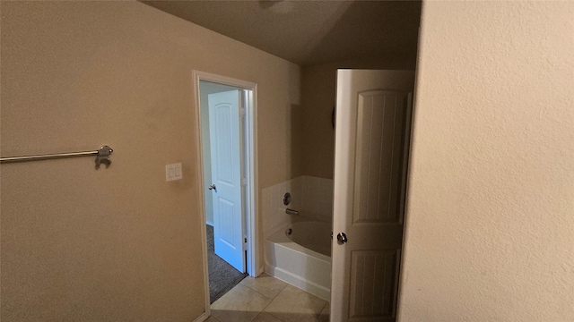 bathroom featuring a bath, a textured wall, and tile patterned floors