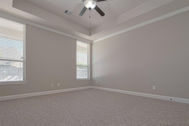 carpeted spare room with ceiling fan, visible vents, baseboards, ornamental molding, and a tray ceiling