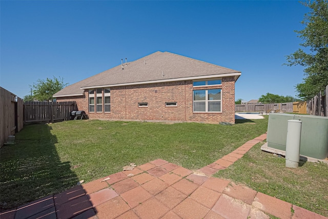 rear view of house featuring a lawn, brick siding, a fenced backyard, a patio, and a shingled roof