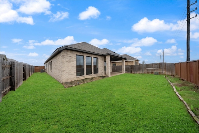 back of property with brick siding, roof with shingles, a fenced backyard, and a lawn