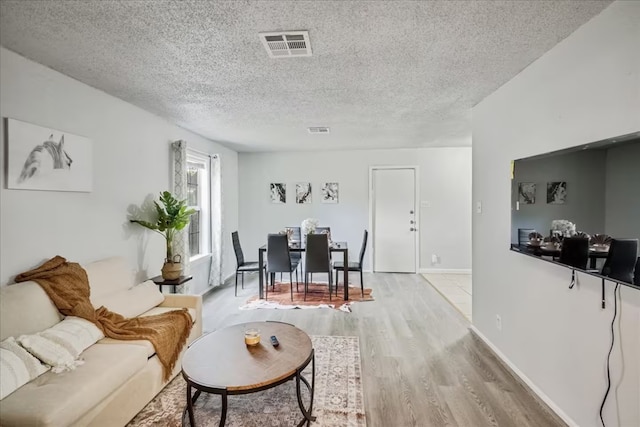 living area featuring light wood-style flooring, a textured ceiling, baseboards, and visible vents