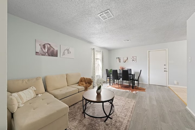 living area featuring a textured ceiling, wood finished floors, baseboards, and visible vents