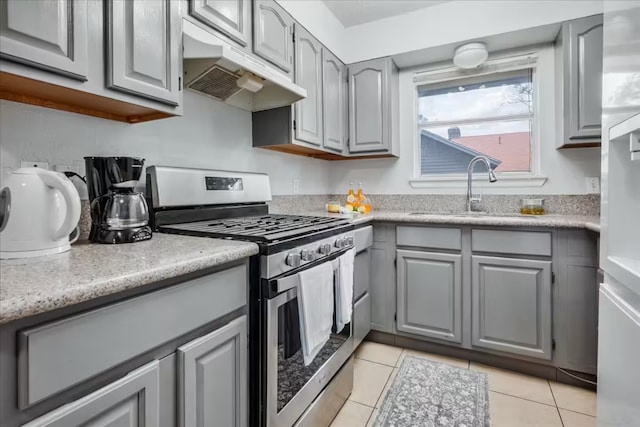 kitchen featuring light tile patterned floors, stainless steel gas range oven, gray cabinetry, under cabinet range hood, and a sink