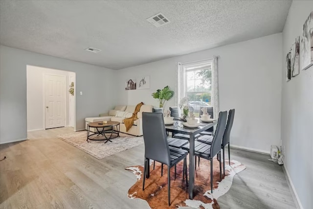 dining space featuring visible vents, a textured ceiling, baseboards, and wood finished floors