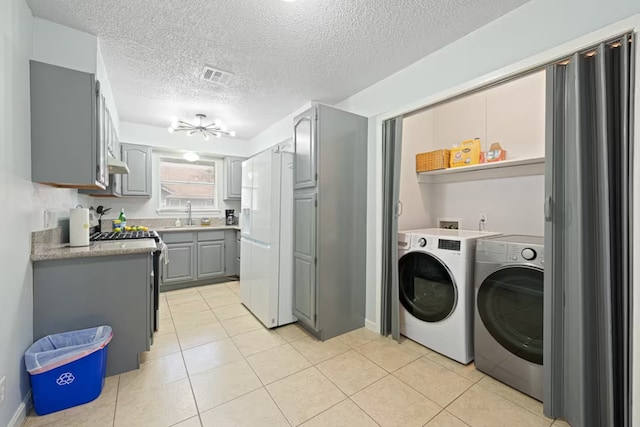 clothes washing area featuring light tile patterned flooring, visible vents, independent washer and dryer, laundry area, and a sink