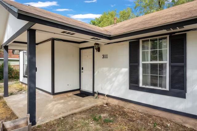 entrance to property with a shingled roof and a patio area