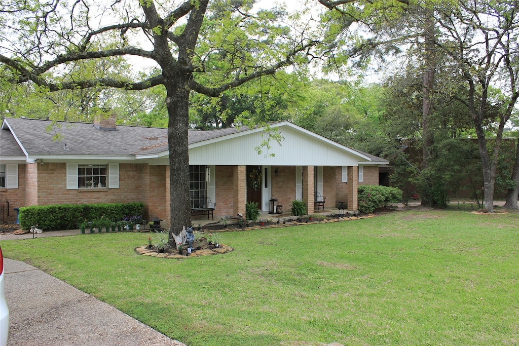 ranch-style house with brick siding, a chimney, a porch, and a front yard