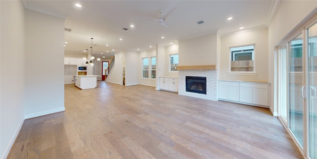 unfurnished living room featuring light wood-style floors, a brick fireplace, baseboards, and crown molding