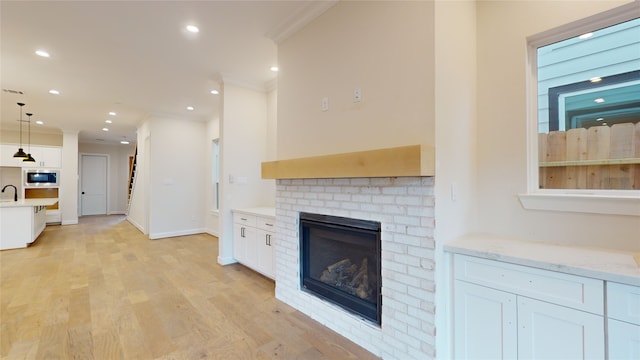 unfurnished living room featuring light wood-type flooring, ornamental molding, recessed lighting, a brick fireplace, and a sink