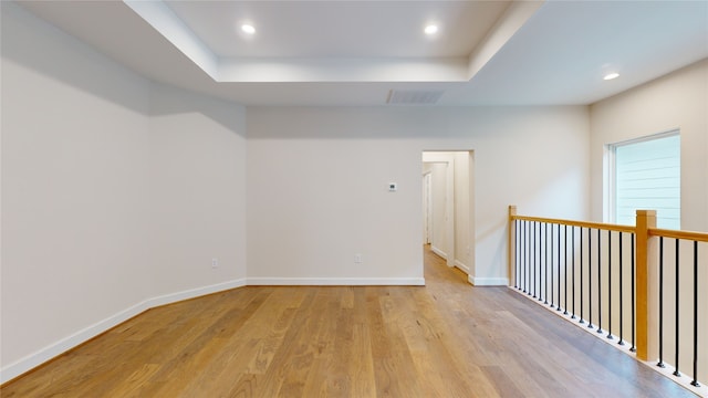 unfurnished room with baseboards, recessed lighting, visible vents, a tray ceiling, and light wood finished floors