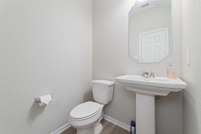 half bathroom with visible vents, baseboards, a sink, toilet, and wood finished floors