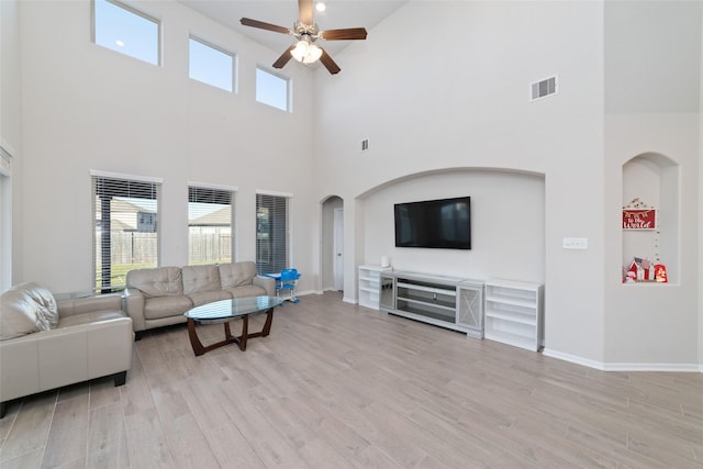 living room with visible vents, ceiling fan, light wood-type flooring, and a towering ceiling