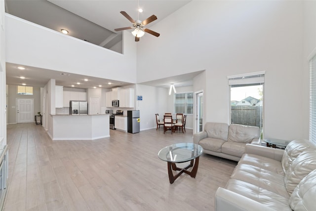 living room featuring baseboards, recessed lighting, a high ceiling, ceiling fan, and light wood finished floors