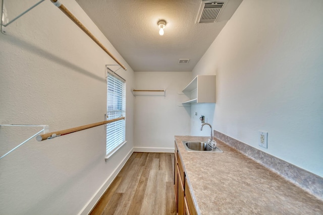 clothes washing area featuring light wood-style flooring, a sink, baseboards, visible vents, and a textured ceiling