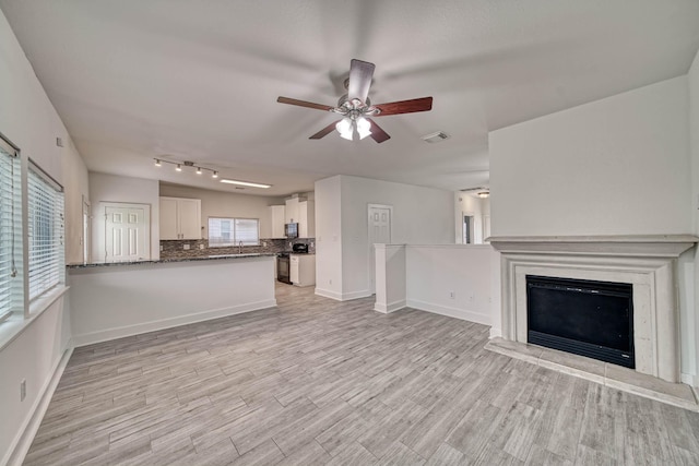 unfurnished living room featuring light wood finished floors, a fireplace with raised hearth, baseboards, visible vents, and a ceiling fan