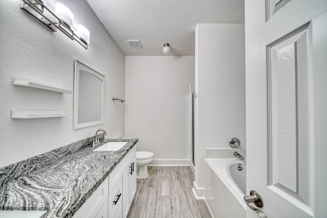 bathroom with vanity, a bath, toilet, visible vents, and wood finished floors