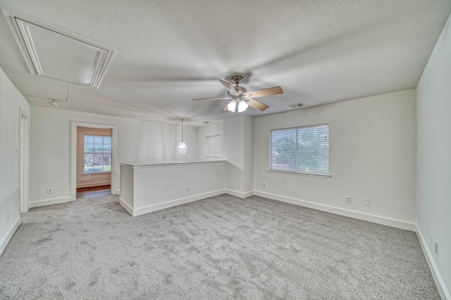 carpeted spare room featuring attic access, a textured ceiling, a ceiling fan, and baseboards