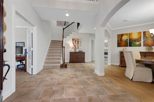 foyer with arched walkways, baseboards, visible vents, ornamental molding, and stairway