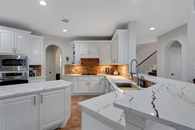 kitchen with arched walkways, a sink, tasteful backsplash, and stainless steel appliances