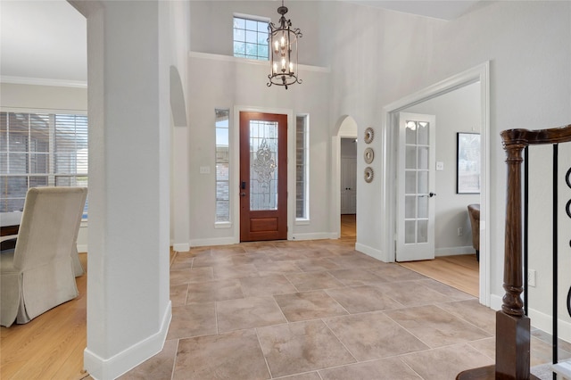 entrance foyer featuring an inviting chandelier, arched walkways, baseboards, and ornamental molding