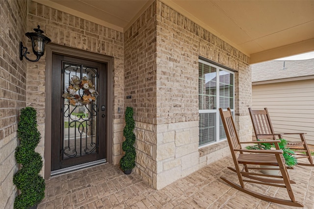 view of exterior entry featuring brick siding and covered porch