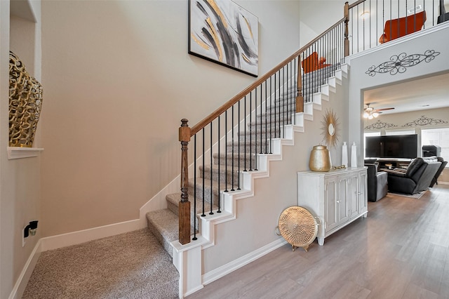 stairs featuring baseboards, ceiling fan, a high ceiling, and wood finished floors