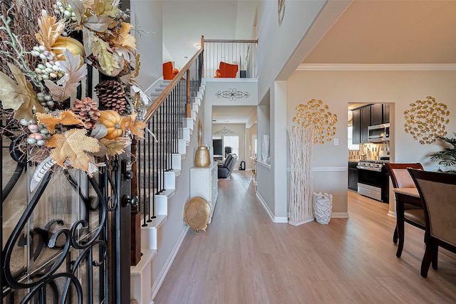 entrance foyer with baseboards, light wood-type flooring, crown molding, a towering ceiling, and stairs
