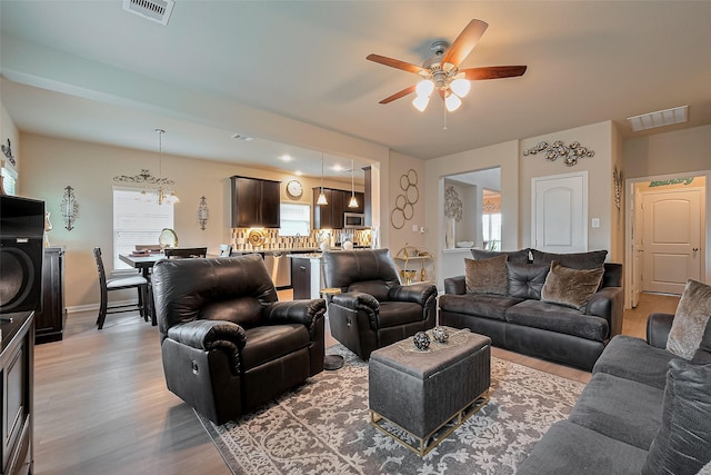 living area with light wood finished floors, visible vents, ceiling fan with notable chandelier, and baseboards