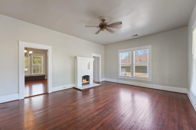 unfurnished living room with plenty of natural light, dark wood finished floors, visible vents, and ceiling fan with notable chandelier