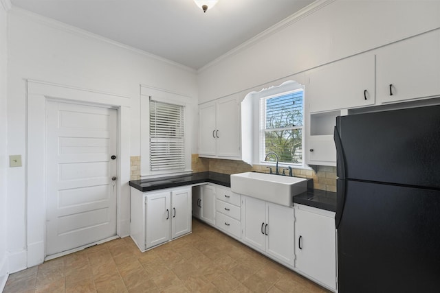 kitchen featuring freestanding refrigerator, dark countertops, a sink, white cabinetry, and crown molding
