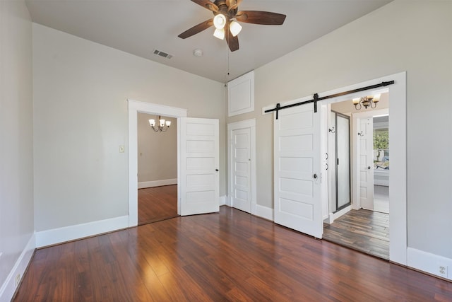unfurnished bedroom featuring visible vents, a barn door, baseboards, wood finished floors, and ceiling fan with notable chandelier