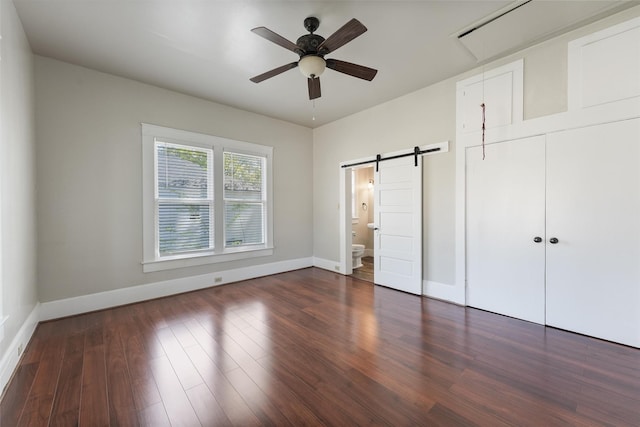 unfurnished bedroom with wood finished floors, connected bathroom, baseboards, and a barn door