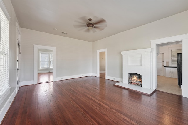 unfurnished living room with ceiling fan, visible vents, baseboards, wood-type flooring, and a brick fireplace