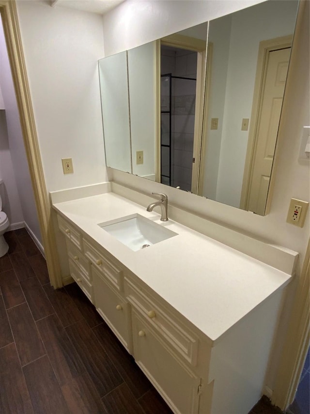 bathroom featuring wood tiled floor, vanity, baseboards, a tile shower, and toilet