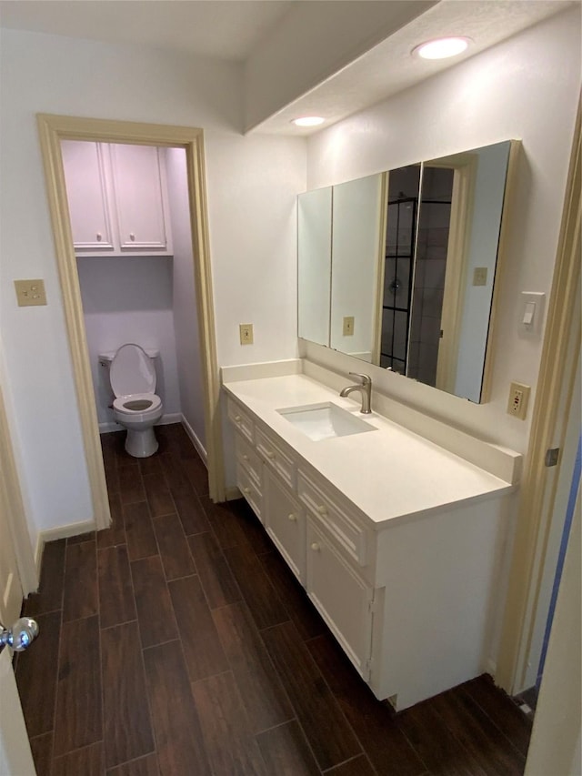 bathroom featuring toilet, baseboards, recessed lighting, wood finished floors, and vanity