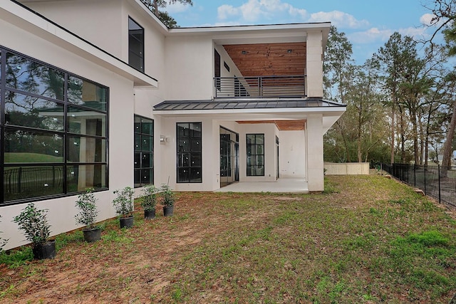 back of property featuring a balcony, stucco siding, a standing seam roof, metal roof, and fence