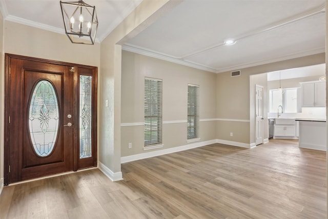 foyer entrance with visible vents, baseboards, a notable chandelier, ornamental molding, and light wood-style flooring