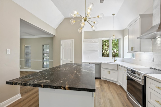 kitchen with light wood-style floors, wall chimney range hood, a sink, stainless steel appliances, and decorative backsplash