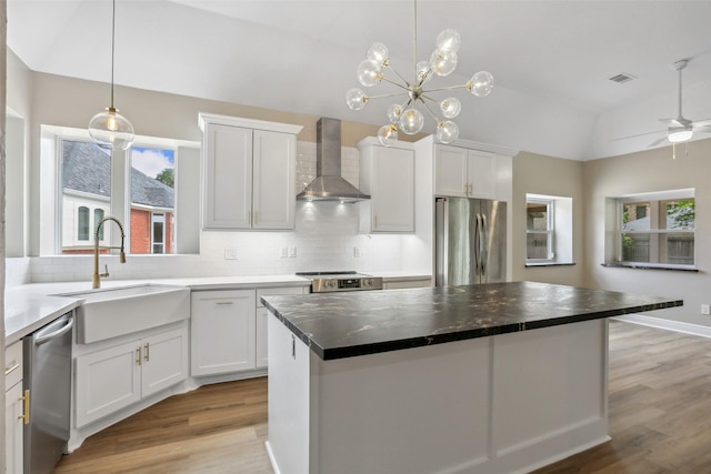 kitchen featuring wall chimney range hood, lofted ceiling, stainless steel appliances, light wood finished floors, and a sink
