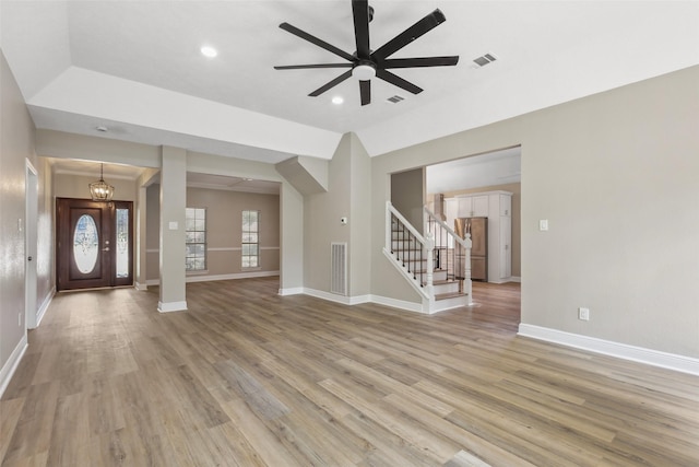 unfurnished living room featuring ceiling fan with notable chandelier, light wood finished floors, visible vents, and stairway