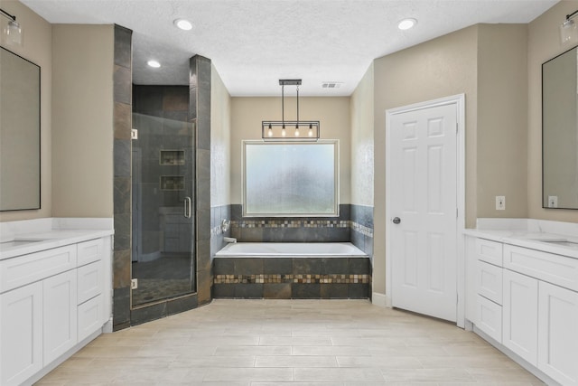 bathroom with a stall shower, a garden tub, two vanities, and visible vents
