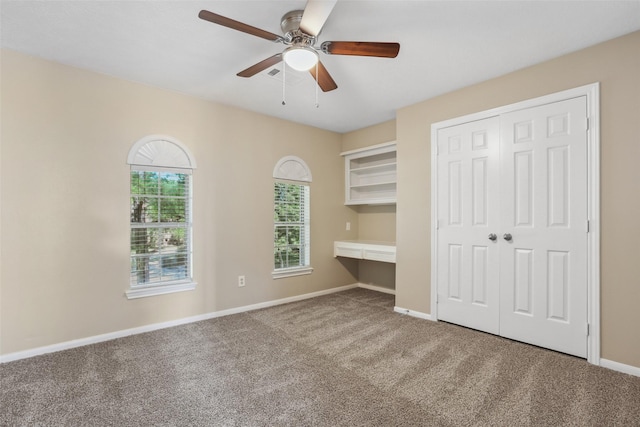 unfurnished bedroom with ceiling fan, a closet, built in desk, carpet flooring, and baseboards